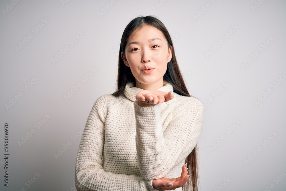 Poster Young beautiful asian woman wearing casual sweater standing over isolated background looking at the camera blowing a kiss with hand on air being lovely and sexy. Love expression.