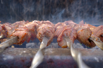Juicy and fresh slices of pork meat are strung on skewers and grilled in charcoal grill. Fragrant smoke. Natural meat dish outdoors on a spring day.