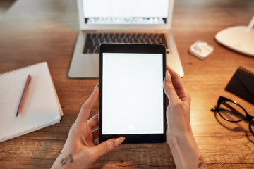 Checking data. Top view of female tattooed hands holding digital tablet under office desk