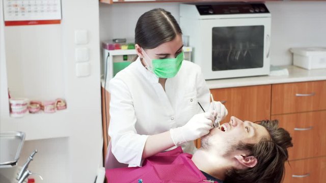 Female doctor in mask and gloves is examining young man's teeth. Dental clinic