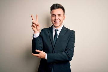 Young handsome business man wearing elegant suit and tie over isolated background smiling with happy face winking at the camera doing victory sign with fingers. Number two.