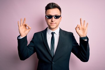 Young handsome caucasian business man wearing funny thug life glasses relax and smiling with eyes closed doing meditation gesture with fingers. Yoga concept.