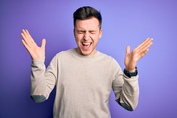 Naklejka premium Young handsome caucasian man wearing casual sweater over purple isolated background celebrating mad and crazy for success with arms raised and closed eyes screaming excited. Winner concept