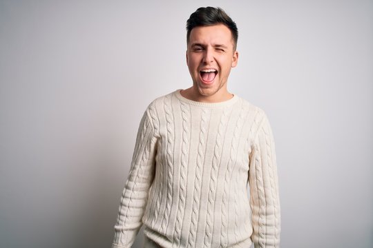 Young handsome caucasian man wearing casual winter sweater over white isolated background winking looking at the camera with sexy expression, cheerful and happy face.
