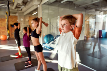 Be alive. Be strong. Be fit. Portrait of boy warming up, exercising with other kids in gym. Stretching on a sunny day. Sport, healthy lifestyle, physical education concept