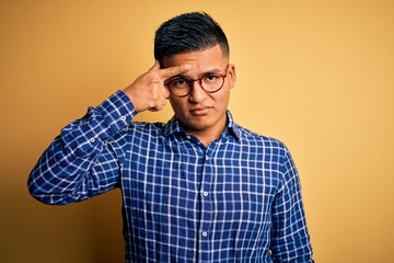 Young handsome latin man wearing casual shirt and glasses over yellow background pointing unhappy...