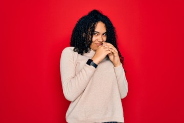 Young african american curly woman wearing casual turtleneck sweater over red background laughing nervous and excited with hands on chin looking to the side