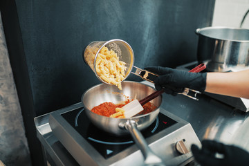 Close up shot of young woman preparing pasta with tomato sous for dinner.
