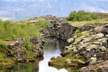 Photo d'un cours d'eau dans une faille du rift islandais marquant la séparation des plaques tectoniques européennes et américaines montrant des roches volcaniques et basaltique recouvertes de mousse