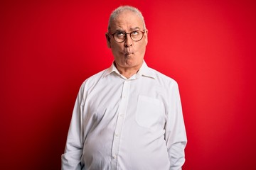 Obraz premium Middle age handsome hoary man wearing casual shirt and glasses over red background making fish face with lips, crazy and comical gesture. Funny expression.