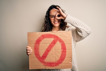 Young beautiful woman with curly hair holding banner with prohibited signal message with happy face...