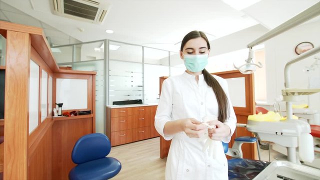 Young attractive nurse in dental clinic is putting on a surgical mask and latex gloves and looking into the camera
