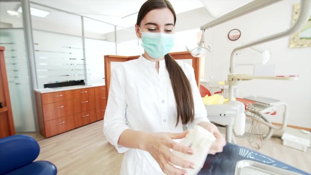 Attractive smiling nurse in dental clinic is putting on a surgical mask and latex gloves and looking into the camera
