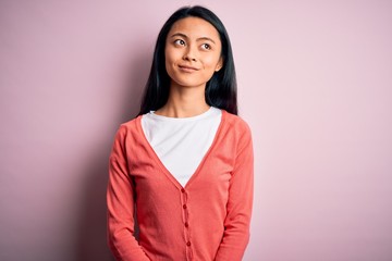 Fototapeta premium Young beautiful chinese woman wearing casual sweater over isolated pink background smiling looking to the side and staring away thinking.