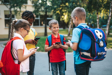 Group of happy elementary school students with smartphones. Primary education, friendship, childhood, and technology concept.