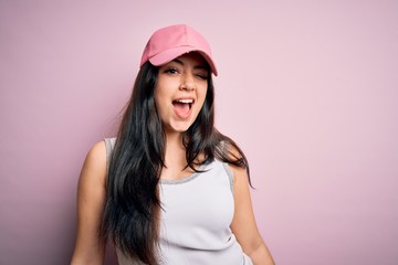 Young brunette woman wearing casual sport cap over pink background winking looking at the camera with sexy expression, cheerful and happy face.