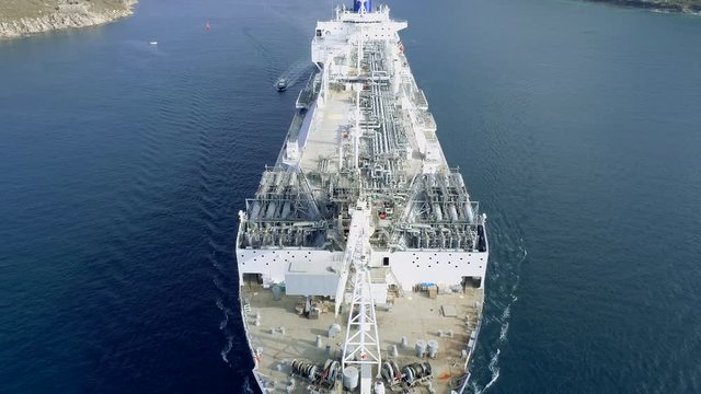 AERIAL DRONE 45 DEGREE CLOSE SHOT AND BACKWARD REVEAL FROM DECK AND PIPES OF AN IMMENSE NATURAL GAS VESSEL, AND FINAL TILT UP AND REVEAL OF BEAUTIFUL NORTH SPAIN ESTUARY WITH GREEN HILLS