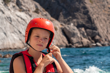 Sports girl in life jacket is standing on seashore and wears red safety helmet for head. Extreme...
