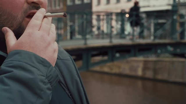 Man smokes real weed joint or medical marijuana or cannabis or hemp near Amsterdam canal, close up