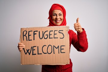 Woman wearing muslim hijab asking for immigration holding welcome refugees message happy with big smile doing ok sign, thumb up with fingers, excellent sign