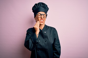 Middle age brunette chef woman wearing cooker uniform and hat over isolated pink background touching mouth with hand with painful expression because of toothache or dental illness on teeth. Dentist