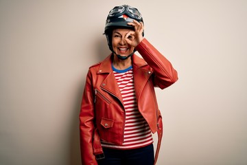 Middle age motorcyclist woman wearing motorcycle helmet and jacket over white background doing ok gesture with hand smiling, eye looking through fingers with happy face.