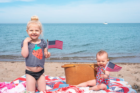 Two little girls at the beach holding American flags - Powered by Adobe