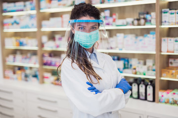 Female pharmacist with protective mask and face shield on her face ,working at pharmacy. Medical healthcare concept.