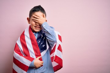 Young little patriotic boy kid covered on united states of america flag on independence day stressed with hand on head, shocked with shame and surprise face, angry and frustrated. Fear and upset