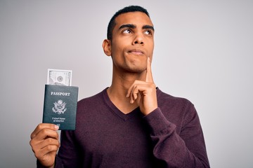 Young handsome african american tourist man holding passport with dollars serious face thinking...