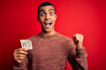 Young handsome african american man holding reminder paper with yes message screaming proud and...