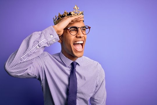 Young Handsome African American Man Wearing Golden Crown Of King Over Purple Background Very Happy And Smiling Looking Far Away With Hand Over Head. Searching Concept.