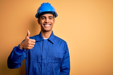Young handsome african american worker man wearing blue uniform and security helmet doing happy...
