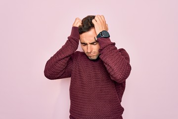 Young handsome man with blue eyes wearing casual sweater standing over pink background suffering from headache desperate and stressed because pain and migraine. Hands on head.