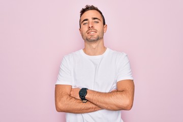 Handsome man with blue eyes wearing casual white t-shirt standing over pink background happy face smiling with crossed arms looking at the camera. Positive person.