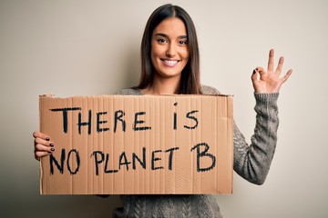 Young beautiful brunette activist woman protesting for save the planet holding banner doing ok sign with fingers, excellent symbol - Powered by Adobe