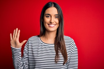 Young beautiful brunette woman wearing casual striped t-shirt over red background showing and pointing up with fingers number five while smiling confident and happy.