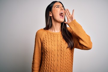 Young beautiful brunette woman wearing casual sweater over isolated white background shouting and screaming loud to side with hand on mouth. Communication concept.