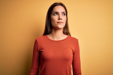 Obraz premium Young beautiful brunette woman wearing casual t-shirt standing over yellow background smiling looking to the side and staring away thinking.