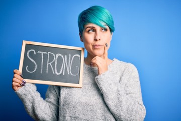 Young woman with blue fashion hair holding blackboard with strong message serious face thinking...