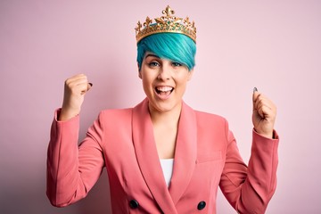 Young business woman with blue fashion hair wearing queen crown over pink isolated background...
