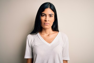 Young beautiful hispanic woman wearing casual white t-shirt over isolated background with serious expression on face. Simple and natural looking at the camera.
