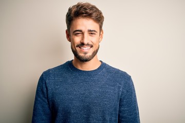 Young handsome man with beard wearing casual sweater standing over white background with a happy...