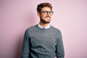 Young handsome man with beard wearing glasses and sweater standing over pink background looking away to side with smile on face, natural expression. Laughing confident. - Powered by Adobe