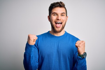 Young handsome blond man with beard and blue eyes wearing casual sweater celebrating surprised and...