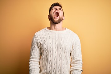 Young blond man with beard and blue eyes wearing white sweater over yellow background angry and mad screaming frustrated and furious, shouting with anger. Rage and aggressive concept.