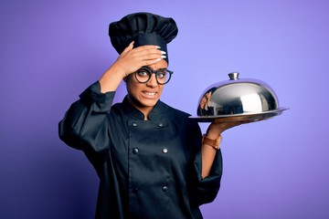 Young african american cooker girl wearing uniform and hat holding tray with dome stressed with hand on head, shocked with shame and surprise face, angry and frustrated. Fear and upset for mistake.