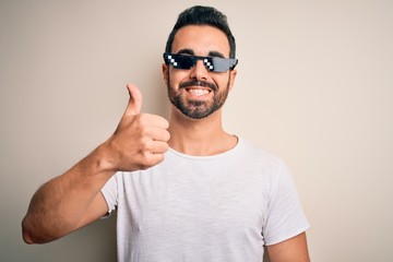 Young handsome man with beard wearing funny thug life sunglasses over white background doing happy...