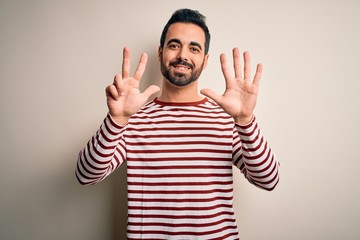 Fototapeta premium Young handsome man with beard wearing casual striped t-shirt standing over white background showing and pointing up with fingers number eight while smiling confident and happy.
