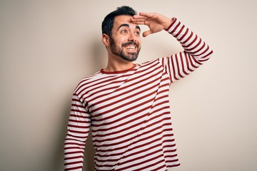 Young handsome man with beard wearing casual striped t-shirt standing over white background very...